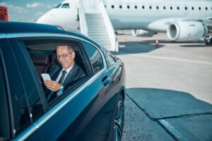 Cheerful businessman with smartphone in car at airport executive airport transfers